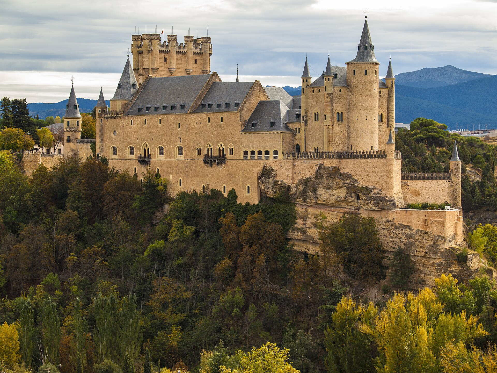 Alcázar de Segovia en otoño, torres y tejados sobre el peñasco arbolado.