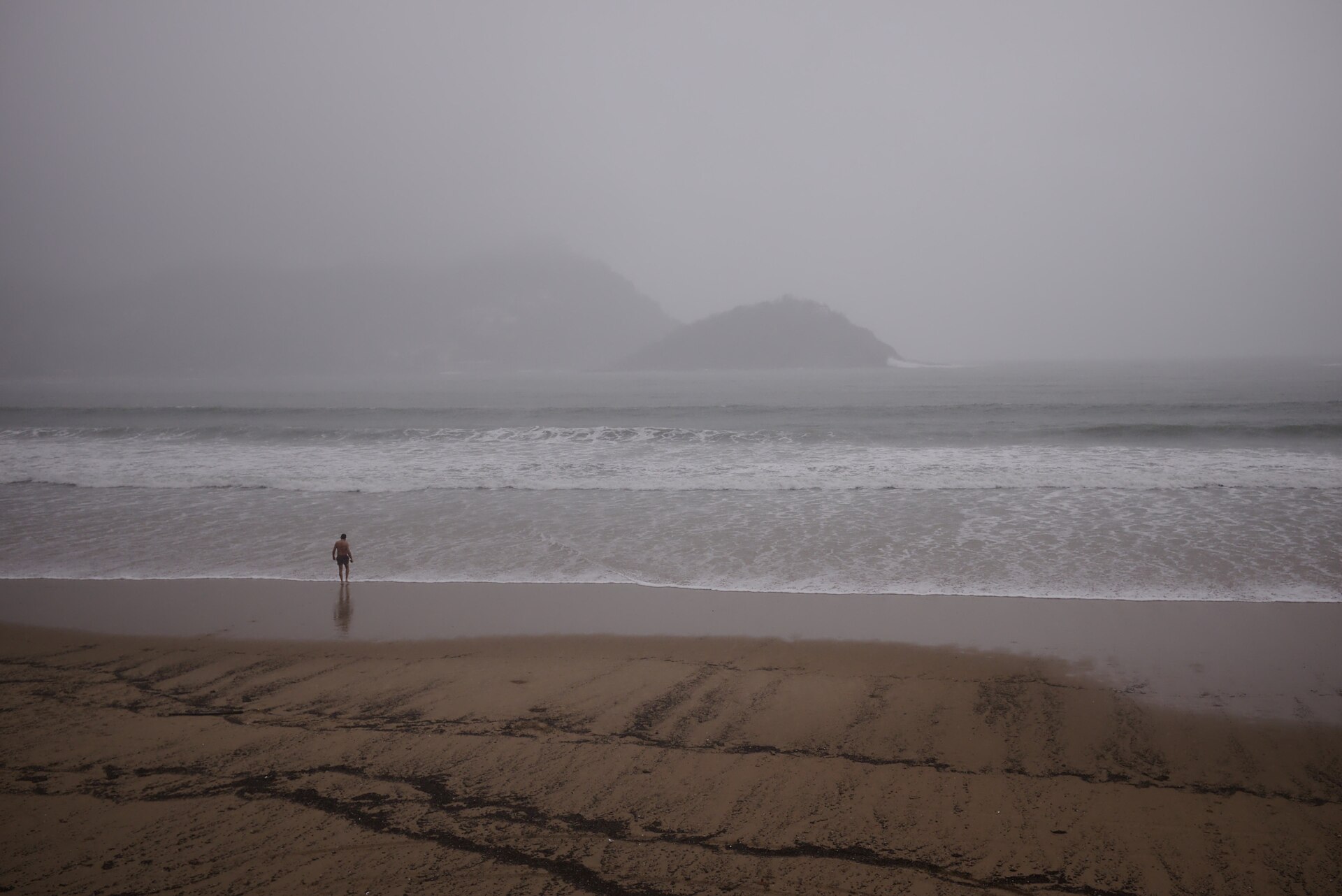 Playa de La Concha con niebla, un bañista solo y la isla de Santa Clara apenas visible.